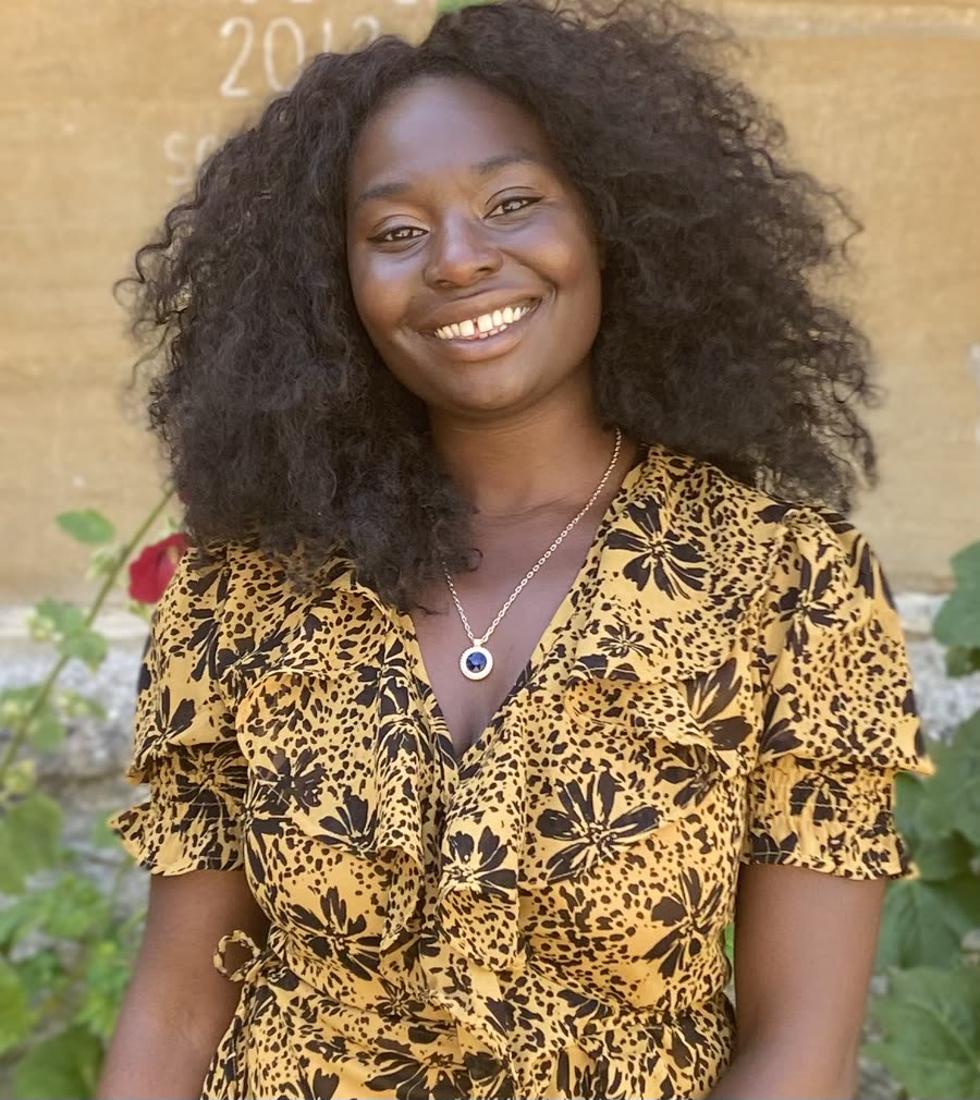 Portrait of Chanju Mwanza smiling, wearing a mustard leopard-print dress